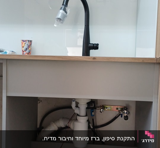 כיור עם ברז וכלי עבודה מתחת לארון מטבח